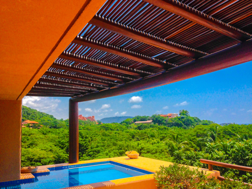 Pérgola de vigas con apariencia de madera frente a alberca y vista a la selva